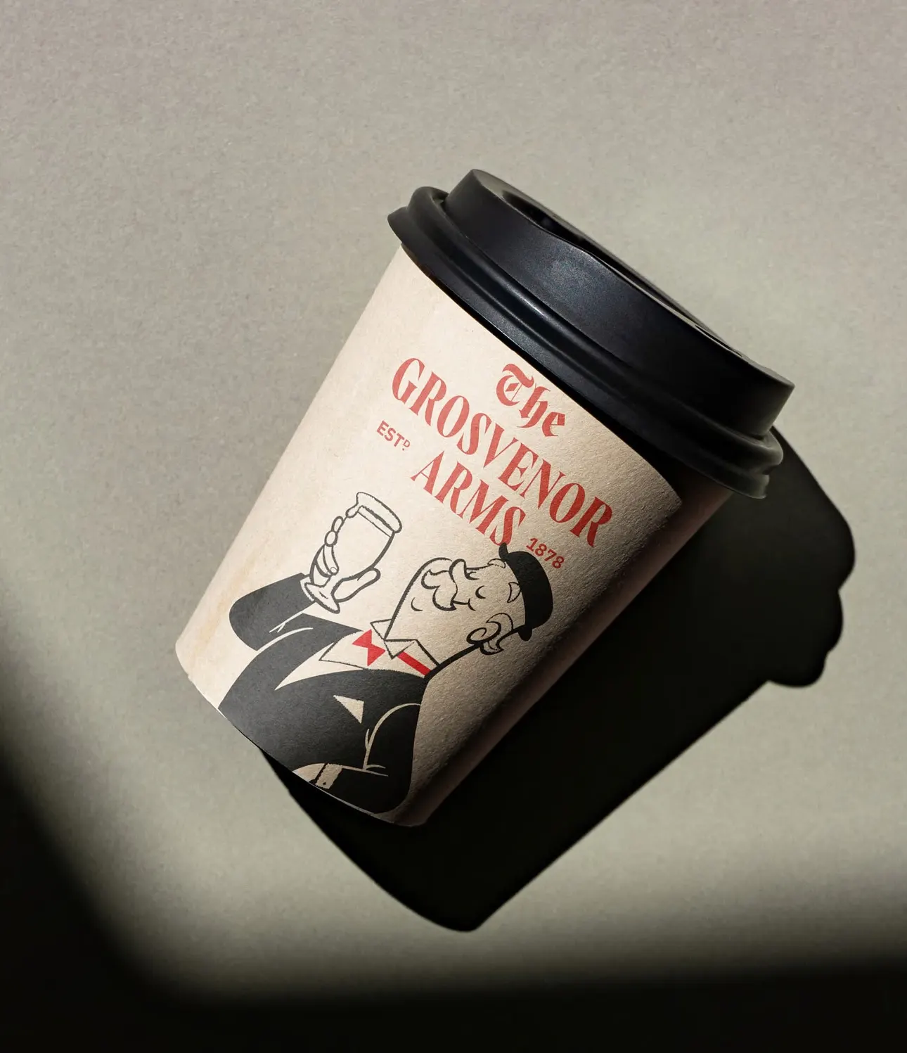 A branded Grosvenor Arms takeaway coffee cup in low sun