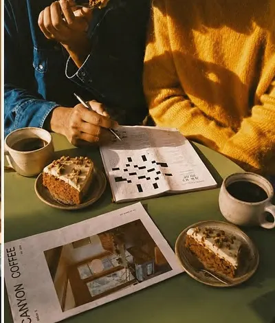 A crossword, two coffees and a slice of carrot cake on a table