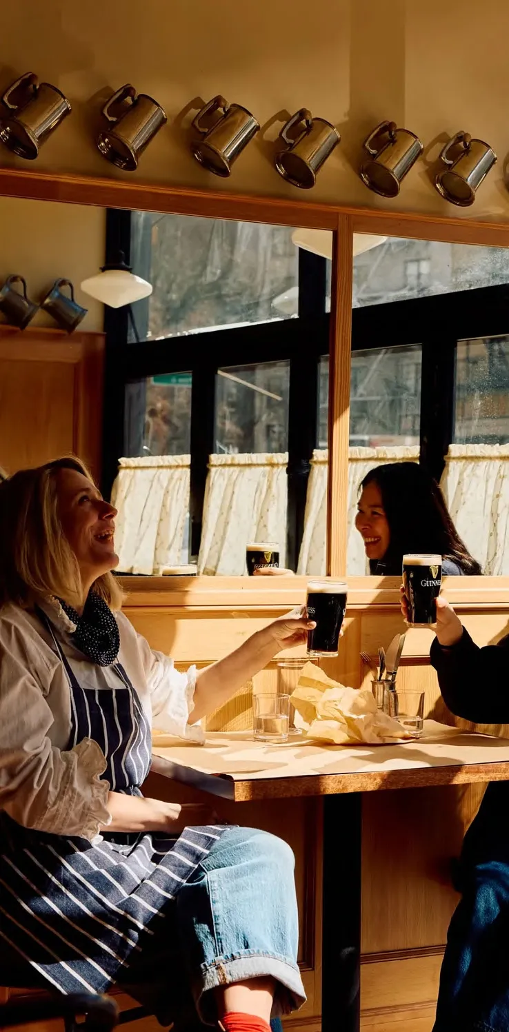 Three guests raising pints at a window table
